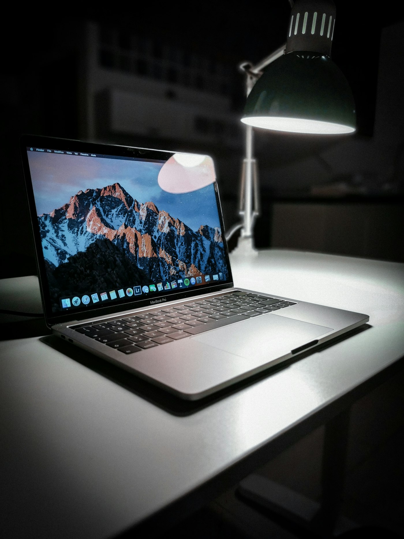 A laptop lit by a desk lamp in a dark, focused workspace
